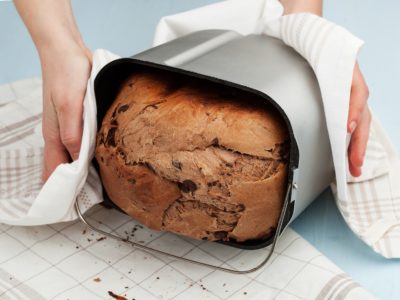 Woman’s hands taking off bread from the breadmaker